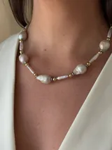 Collar corto de perlas de río alargadas y ovaladas, con cuentas de acero quirúrgico y bolitas con baño de oro. Cierre con cadena de acero quirúrgico y gancho para regular el largo.