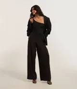 Pantalón pantalona de sastrería color negro, confeccionado en tejido texturizado. Presenta corte amplio, superposición lateral con lazo y tiro alto.