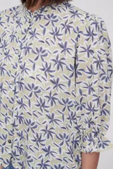 Blusa estampada con flores azules y hojas verdes, cuello mao con volados, mangas 3/4 con volados en los puños y cierre frontal con botones.