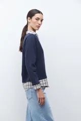 Sweatshirt azul marino de manga larga con cuello en V, superpuesto a una camisa de cuadros beige y azul que asoma en el cuello, puños y ruedo.