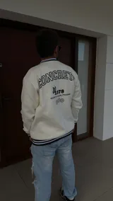 Buzo color crema con cuello, puños y cintura acanalados con rayas negras. Estampado en la espalda con la palabra "CONCRETE" en mayúsculas, el número "1978", un conejo y la frase "SOUND & VISUAL PROGRAM".