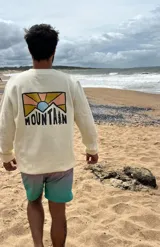 Buzo color crema de corte clásico con estampa en la espalda con un paisaje de montaña y la palabra "Mountain" en tipografía sans-serif.