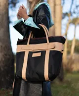 Bolso de playa de lona color verde claro con detalles en cuero color beige. Tiene doble asa de hombro y cierre superior con tira de cuero.