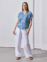 Blusa celeste estampada con motivos de playa, con cuello a la base y escote en V. Mangas cortas con detalle fruncido.