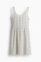 Vestido corto de breteles finos, confeccionado en tejido de punto blanco con estampado floral en negro. El cuerpo es entallado con escote redondo y costura fruncida en la cintura. La falda es levemente acampanada.