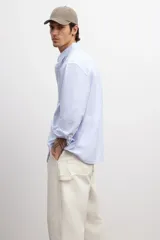 Camisa de vestir celeste y blanco a rayas verticales, de corte regular fit, con cuello abotonado, bolsillo en el pecho y mangas largas con puños abotonados.