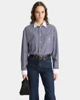 Camisa celeste claro a rayas verticales con cuello y puños blancos, corte oversized y bolsillo en el pecho con logo bordado.
