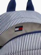Mochila Tommy Jeans Essential con diseño a rayas verticales azules y blancas, base color beige, asa superior y correas acolchadas ajustables. Cuenta con compartimento principal con cierre de cremallera, bolsillo interior de malla y bolsillo exterior con cremallera.