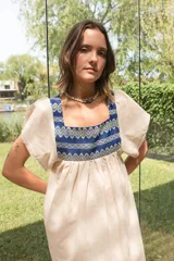 Túnica color beige de lino con cuello cuadrado y mangas cortas. Presenta apliques de textiles antiguos en la pechera delantera y trasera con motivos geométricos en color azul.