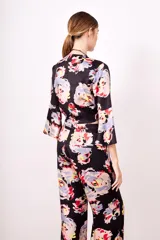 Camisa estampada con flores de colores sobre fondo negro, de corte cruzado, mangas 3/4 acampanadas y escote en V.