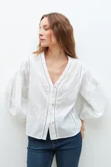 Blusa lila con bordados, de mangas largas abullonadas y cuello en V.