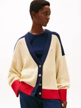 Cárdigan de punto color crema, con cuello en V, cierre con botones y corte amplio. Presenta detalles en azul marino en los hombros y en el borde del cuello, y detalles en rojo en los puños y en el ruedo. Logo de Tommy Hilfiger bordado en el pecho.