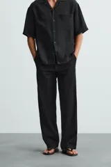 Pantalón negro de corte recto y calce relajado, confeccionado en tejido de algodón con elasticidad. Presenta cintura ajustable con cordón, bolsillos frontales y bolsillos traseros de doble vivo.