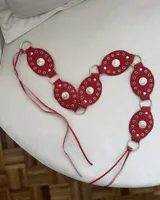 Cinto rojo con apliques metálicos plateados y tiras para atar.