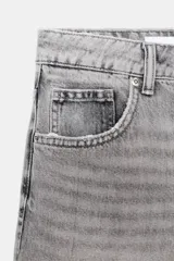 Shorts de denim gris claro con efecto lavado, tiro bajo y corte ancho (baggy). Presenta cinco bolsillos y cierre frontal con cremallera y botón metálico.