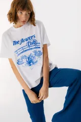 Remera blanca de algodón con estampado de tres jarrones con flores rojas y la frase "The Flowers Club" en azul.
