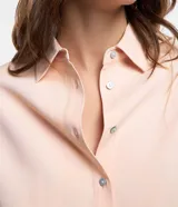 Camisa color rosa pálido, de corte amplio y alargado, confeccionada en viscosa. Tiene cuello camisero, abotonadura frontal y mangas largas con puños abotonados.