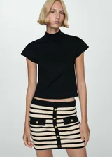 Minifalda de punto a rayas horizontales en color crema y negro, con ribetes en contraste. Presenta dos bolsillos de solapa con botón dorado en la parte delantera y botones decorativos.