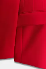 Blazer roja de corte recto, con cuello smoking de satén negro, mangas largas con hombreras, bolsillos frontales con solapa y cierre frontal con un botón.