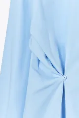 Camisa celeste de corte holgado, con cuello solapa, manga larga y cierre frontal con botones. Presenta detalle de cintura ajustable con botones.