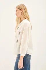 Camisa blanca de voilé de algodón con escote redondo y bordados de ojos en el delantero. De corte recto y mangas largas con puños abotonados.