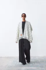 Ruana color crudo con diseño de cuadros negros y flecos en el borde inferior.