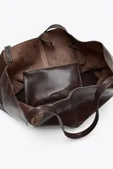Bolso maxi shopper de cuero color marrón oscuro, con pespuntes a tono y asas de hombro. Incluye cierre con tiras y botón, y cartera con bolsillo extraíble.