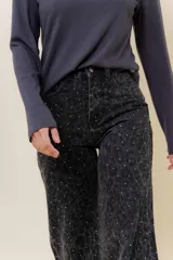 Pantalón de jean negro de pierna ancha y tiro medio-alto, con estampado sutil de leopardo en tono más oscuro y pequeños puntos blancos brillantes.