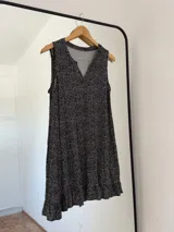 Vestido corto negro con estampado de lunares blancos, escote en V y sin mangas.
