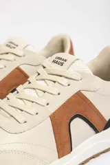 Zapatillas deportivas marrones con detalles en blanco y suela color caramelo.