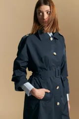 Trench color beige de corte clásico con cuello amplio, botones frontales, detalles en los hombros y mangas largas.