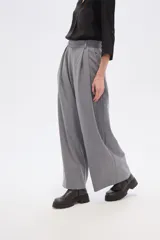 Pantalón gris de poliéster, de corte baggy, tiro alto, con pinzas frontales y bolsillos laterales.