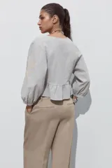 Blusa corta color celeste con textura arrugada, escote en V con puntilla, lazo ajustable en el frente y mangas 3/4 abullonadas con bordados florales a contraste.