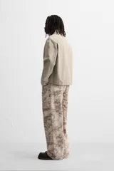 Pantalón de jean de corte recto con estampado abstracto en tonos beige, marrón y gris.