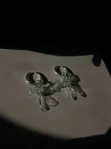 Par de aros colgantes con argollas de acero inoxidable y dijes de vidrio soplado con forma de moño, disponibles en color celeste y rosa.