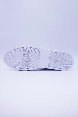 Zapatilla urbana de caña baja, color blanco, con cordones y suela de goma blanca. El cuerpo del calzado presenta microperforaciones y un logo de pingüino en relieve en el lateral.