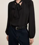Blusa negra de crepé con cuello con lazo, mangas largas y pliegues en los hombros.