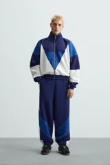 Pantalón deportivo azul marino con paneles laterales blancos y detalles en azul eléctrico. Corte relaxed fit, cintura elástica ajustable con cordón, bolsillos frontales ocultos y puños elásticos.
