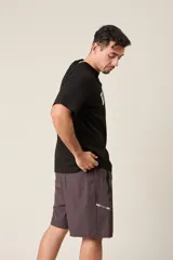 Bermuda deportiva gris de nylon, de corte suelto, con cintura elástica y cordón de ajuste. Cuenta con detalles de líneas negras en los costados y bolsillos laterales con cierre.