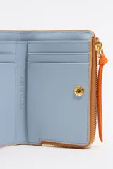 Monedero negro de piel con estructura rígida, logo metálico dorado, tirador de cordón y acabados metálicos dorados. Tarjetero interior, cierre con botón de presión e interior con logo grabado. Confeccionada en 100% poliéster reciclado y 100% poliuretano de producción responsable.