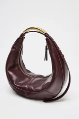 Bolso de mano ovalado color marrón oscuro, con asa de hombro metálica dorada y cierre superior con cremallera.