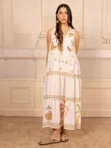 Vestido largo color crema con estampado de flores y corazones en tonos azules, naranjas y amarillos. Tiene cuello en V con ribete azul y corte imperio con falda escalonada.