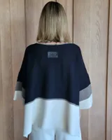 Buzo de punto con mangas 3/4, corte amplio y diseño a bloques de color negro, gris y blanco.