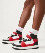 Championes de caña alta, color blanco, rojo y negro, con ajuste de cordones y velcro. Suela bicolor y puntera redondeada.