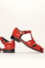 Sandalia roja de cuero vacuno con diseño de tiras entrecruzadas y hebilla lateral. Tiene suela de cuero artesanal y taco bajo.