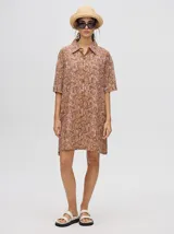 Camisa vestido corto con estampado abstracto en tonos marrones y lilas. Tiene cuello camisero, mangas cortas y cierre frontal con botones.