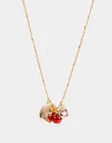 Collar corto dorado con cadena de eslabones y dijes colgantes: moneda dorada con letras NY grabadas, dos manzanas rojas esmaltadas y dije redondo dorado con corazón rosa.