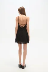 Vestido corto negro, con escote profundo en V, tirantes finos y falda con terminación en tela transparente.