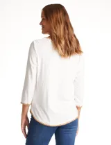 Remera de modal color blanco, con cuello redondo y mangas 3/4. Presenta un aplique bordado en color tostado en el cuello, los puños y el ruedo.