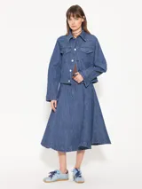 Campera de denim azul con textura en relieve, corte recto, cuello camisero, cierre frontal con botones blancos, bolsillos delanteros y mangas largas con pinzas que generan volumen.